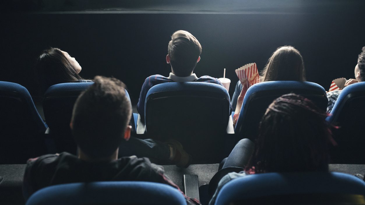Des personnes regardent un film au cinéma, vus de dos.