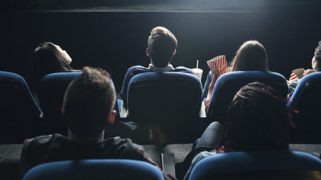 Des personnes regardent un film au cinéma, vus de dos.