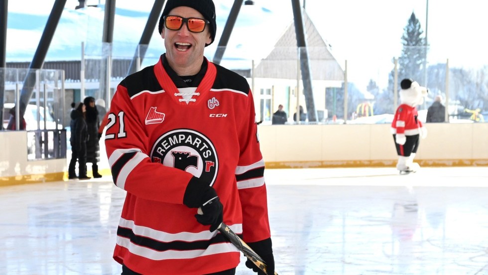 Le maire de Québec, Bruno Marchand, sur une patinoire portant un chandail des Remparts et tenant un bâton de hockey.