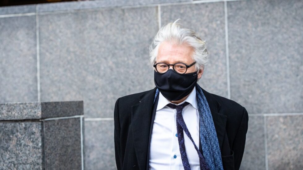 Gilbert Rozon portant un masque devant un mur du palais de justice de Montréal.