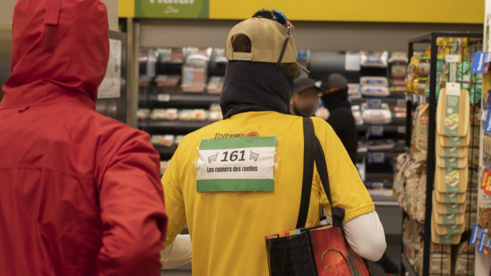 Deux membres des Robins des Ruelles vus de dos dans une épicerie Maxi.