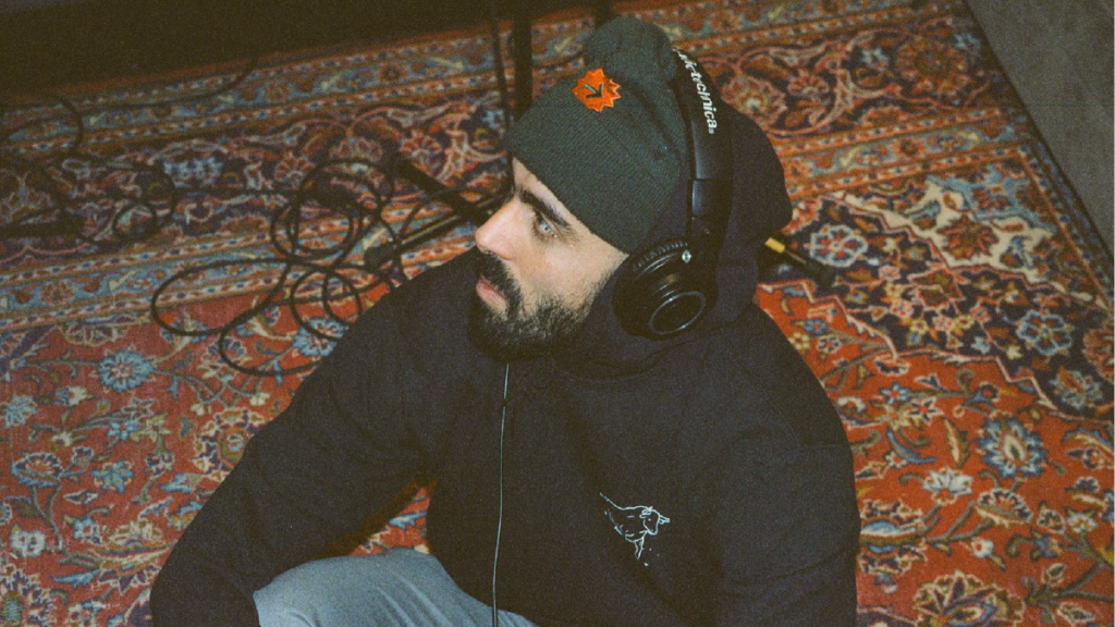 L'humoriste Adib Alkhalidey assis sur un tapis avec un casque d'écoute sur la tête.