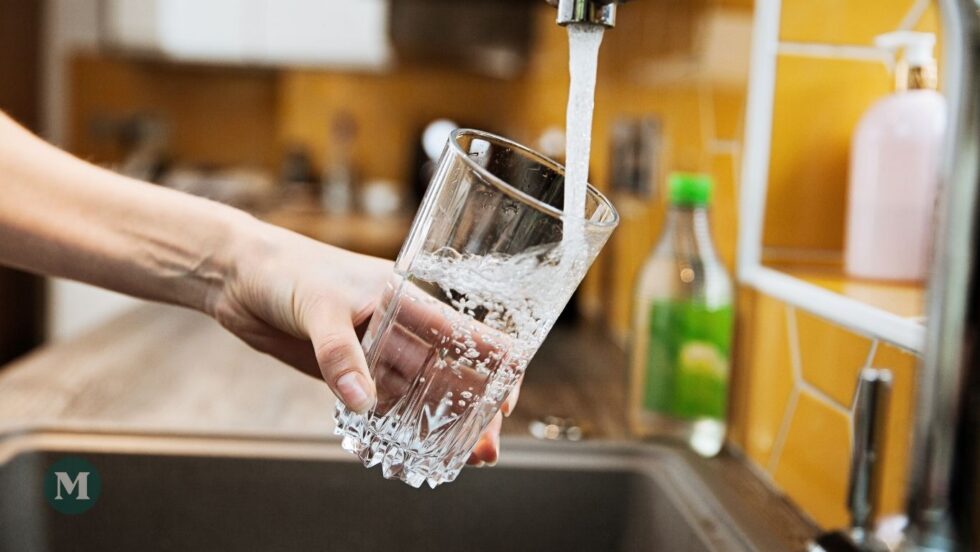 Une femme remplit un verre d'eau au robinet de la cuisine.